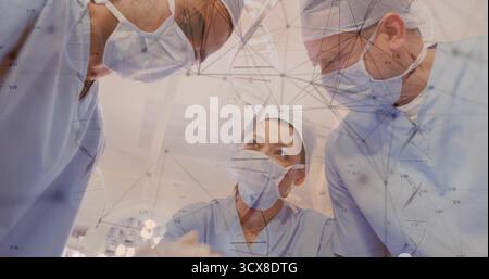 Discussing three surgeons leaning over patient at OR table in operating room, with network overlay Stock Photo