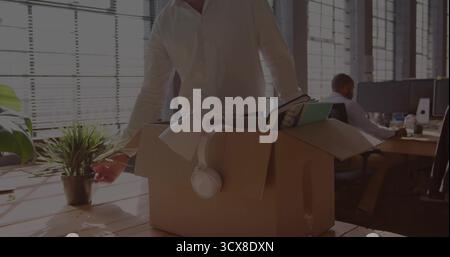 Packing items senior male office worker placing plant, lamp and headphones into box at wooden desk Stock Photo