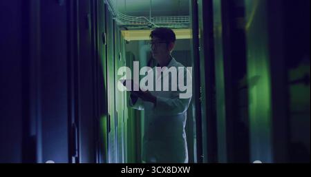 Technician wearing white lab coat inspecting server racks and trays in server room using tablet Stock Photo