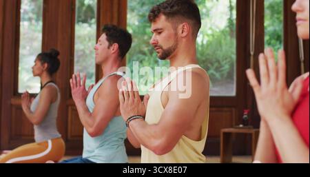 Practicing kneeling prayer pose bearded man in tank top yoga studio with yoga mats, copy space Stock Photo