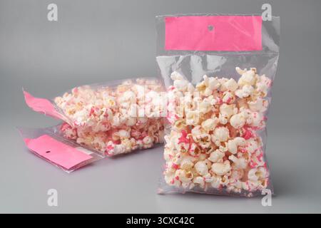 stack of sweetened popcorn in clear plastic packets, pink sugar dusting on white snack, sealed bag with blank label isolated gray background, concept Stock Photo