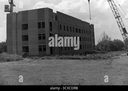A dynamic archival photo from the 1980s shows a major construction project in Sloviansk, Ukrainian SSR. The focus is a large, multi-story brick building with its structural shell complete, evidenced by the empty window openings. A massive construction crane looms over the site, while stacks of bricks and concrete panels lie in the foreground. This image powerfully captures a moment of urban expansion and industrial labor, a snapshot of a peaceful Donbas focused on building its future before the war Stock Photo
