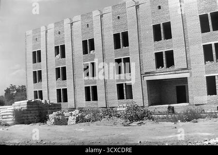 A dynamic archival photo from the 1980s shows a major construction project in Sloviansk, Ukrainian SSR. The focus is a large, multi-story brick building with its structural shell complete, evidenced by the empty window openings. A massive construction crane looms over the site, while stacks of bricks and concrete panels lie in the foreground. This image powerfully captures a moment of urban expansion and industrial labor, a snapshot of a peaceful Donbas focused on building its future before the war Stock Photo