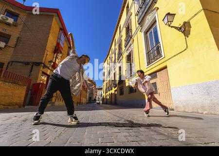 Two young male dancers performing contemporary street dance move on a sunny cobblestone street, expressing dynamic motion and urban culture against ye Stock Photo