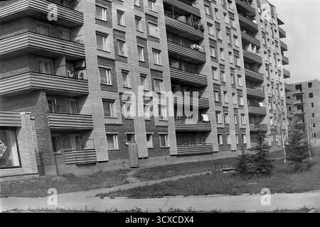 An atmospheric black and white archival photo from the 1980s, showing a residential building on Svobody Street in Sloviansk, Ukrainian SSR. The image perfectly captures the essence of late-Soviet architecture with its textured brick facade, strong geometric patterns, and uniform rows of balconies. Along the sidewalk, newly planted young fir trees and classic Soviet-era streetlights stand as symbols of recent urban development. The scene portrays a quiet, everyday moment in a typical socialist city, a valuable historical record of peaceful urban growth and daily life in Donbas before the war Stock Photo