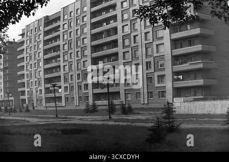 An atmospheric black and white archival photo from the 1980s, showing a residential building on Svobody Street in Sloviansk, Ukrainian SSR. The image perfectly captures the essence of late-Soviet architecture with its textured brick facade, strong geometric patterns, and uniform rows of balconies. Along the sidewalk, newly planted young fir trees and classic Soviet-era streetlights stand as symbols of recent urban development. The scene portrays a quiet, everyday moment in a typical socialist city, a valuable historical record of peaceful urban growth and daily life in Donbas before the war Stock Photo