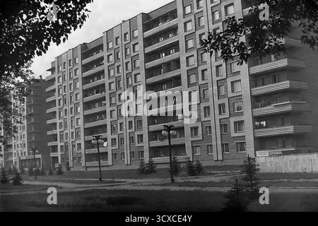 An atmospheric black and white archival photo from the 1980s, showing a residential building on Svobody Street in Sloviansk, Ukrainian SSR. The image perfectly captures the essence of late-Soviet architecture with its textured brick facade, strong geometric patterns, and uniform rows of balconies. Along the sidewalk, newly planted young fir trees and classic Soviet-era streetlights stand as symbols of recent urban development. The scene portrays a quiet, everyday moment in a typical socialist city, a valuable historical record of peaceful urban growth and daily life in Donbas before the war Stock Photo