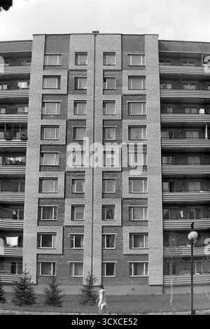 An atmospheric black and white archival photo from the 1980s, showing a residential building on Svobody Street in Sloviansk, Ukrainian SSR. The image perfectly captures the essence of late-Soviet architecture with its textured brick facade, strong geometric patterns, and uniform rows of balconies. Along the sidewalk, newly planted young fir trees and classic Soviet-era streetlights stand as symbols of recent urban development. The scene portrays a quiet, everyday moment in a typical socialist city, a valuable historical record of peaceful urban growth and daily life in Donbas before the war Stock Photo