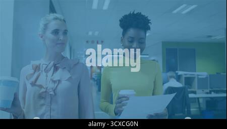 Walking two colleagues wearing blouse, yellow top, reviewing document in open-plan office corridor Stock Photo