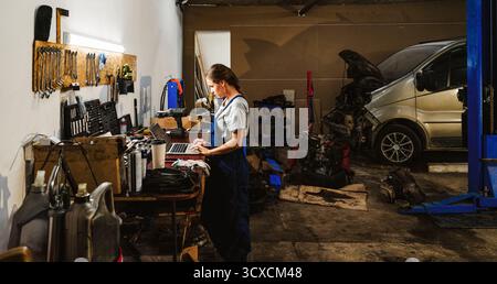 Female worker using laptop in local auto repair shop. Stock Photo