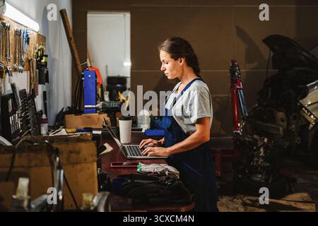 Female worker using laptop in local auto repair shop. Stock Photo
