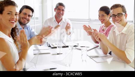 Applauding group of six professionals seated around conference table in office with notebooks, pens Stock Photo