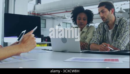Leaning colleagues working over silver laptop and graphics tablet in office, holding stylus pens Stock Photo