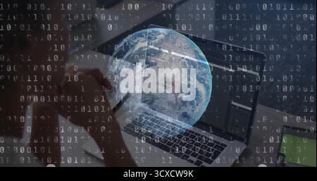 Typing mid-adult woman entering code on laptop at office desk, holding smartphone with binary globe Stock Photo