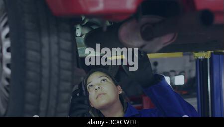 Mechanic wearing coveralls black gloves checking exhaust under lifted red car at garage Stock Photo