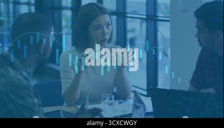 Discussing three colleagues analyzing financial trends in office with laptops, candlestick overlay Stock Photo