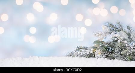 Snow-covered evergreen branches in the foreground with soft glowing bokeh lights in the background. Stock Photo