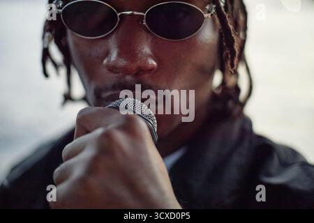 Portrait of Young Adult Black Man Singing into Microphone Outdoors Stock Photo
