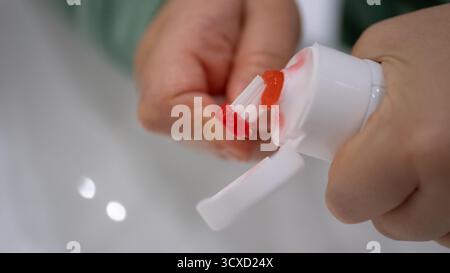 Extreme close-up of toothpaste being squeezed onto a red toothbrush. Real-life morning hygiene scene, focused on authentic home detail. Conceptual ima Stock Photo