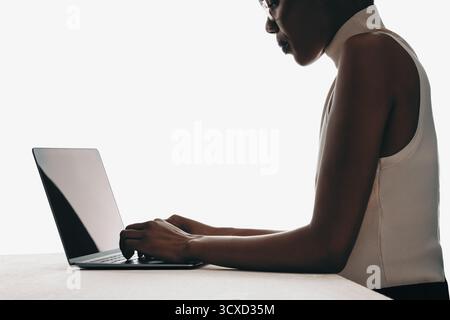 Side profile of a woman focused on typing on a laptop displaying professional engagement. Stock Photo