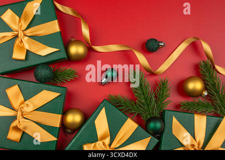 Green gift boxes with golden bows on red background. Gift boxes,  fir tree branches, Christmas balls and golden ribbon  on red. Stock Photo
