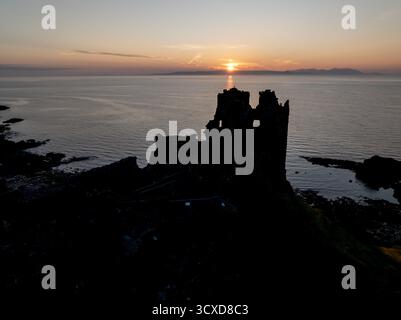 Aerial sunset view of Dunure Castle in South Ayrshire, Scotland, showing the ruined coastal fortress in silhouette against a dramatic evening sky. Stock Photo