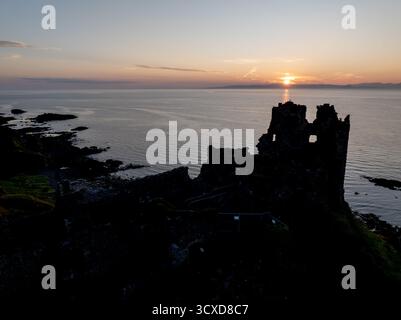Aerial sunset view of Dunure Castle in South Ayrshire, Scotland, showing the ruined coastal fortress in silhouette against a dramatic evening sky. Stock Photo