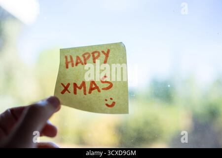 Hand posting a handwritten happy xmas greeting on a window with a smiley face Stock Photo