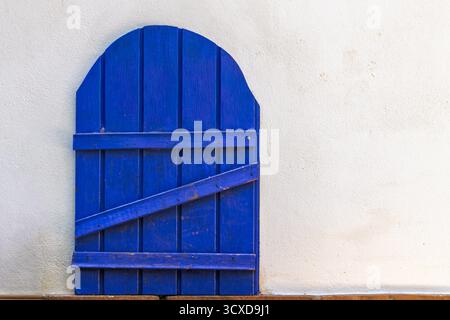 Blue wooden door with an arched top, closed against a textured white wall. Rustic architecture detail for design projects Stock Photo