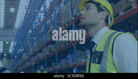 Supervisor wearing yellow hard hat, vest checking shelves in warehouse aisle with boxes, copy space Stock Photo