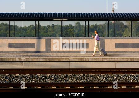 Elegant businesswoman walking confidently with suitcase and using mobile at the train station. Copy space for your text or advertisement. Stock Photo