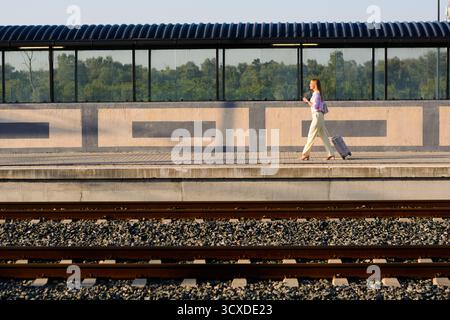 Elegant businesswoman walking confidently with suitcase and using mobile at the train station. Copy space for your text or advertisement. Stock Photo