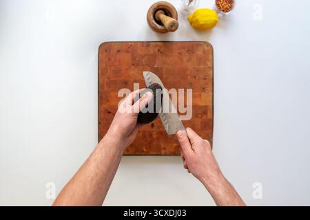 Top view of hands slicing ripe avocado with knife on cutting board. Guacamole ingredients: lemon, spices. Healthy food preparation. Fresh and natural Stock Photo
