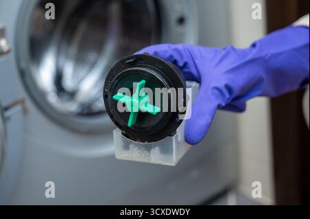 Close-up of a person wearing purple gloves holding a washing machine drain pump motor with a green impeller, demonstrating appliance maintenance or pa Stock Photo