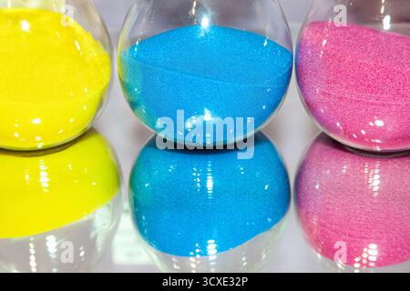 Tree glass hourglass flasks containing yellow, red and blue sand Stock Photo