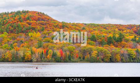 A lone kayaker paddles along the Gatineau river reflected in water, on a beautiful fall day in Quebec, Canada Stock Photo