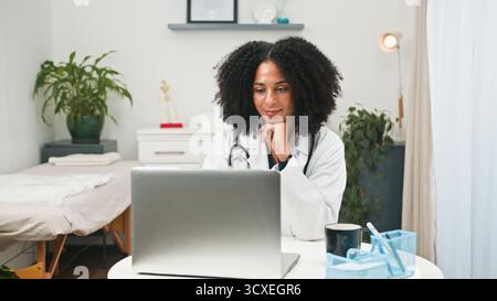 Focused Female Doctor Using Laptop In Modern Clinic Office With Stethoscope And Plants Stock Photo