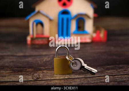 Padlock and keys placed in front of a small wooden house model on dark wooden table, representing property protection, mortgage. Stock Photo