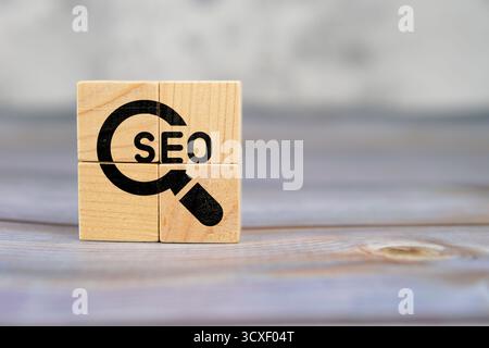SEO text with magnifying glass icon printed on wooden cubes placed on a wooden desk, symbolizing search engine optimization. Stock Photo