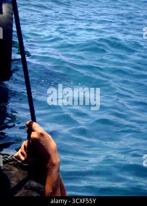 hands hanging from a rope on a pier by the sea Stock Photo