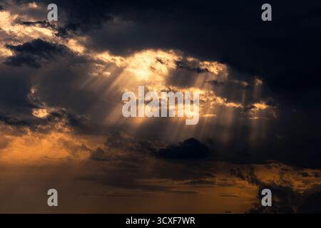 Sun rays shining through dramatic clouds at sunset Stock Photo