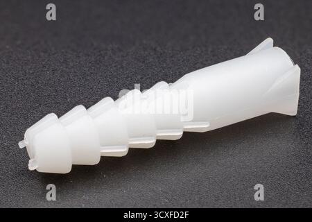 Side-angle view of a white plastic wall anchor on a dark, textured background Stock Photo