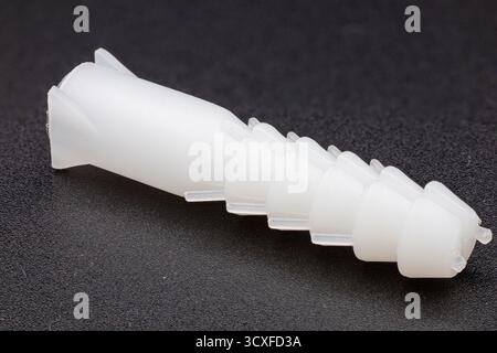 Side-angle view of a white plastic wall anchor on a dark, textured background Stock Photo