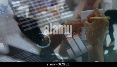 Holding yellow pencil, analyst writing notes on notepad in office, with overlaid financial charts Stock Photo