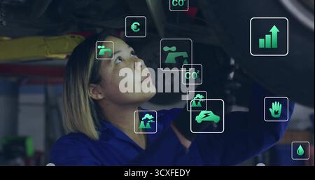 Inspecting mechanic in blue coverall and gloves under vehicle in garage with floating data icons Stock Photo