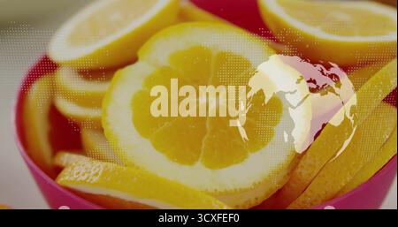 Displaying lemon slices in red bowl on white table, with dotted world map overlay and globe Stock Photo