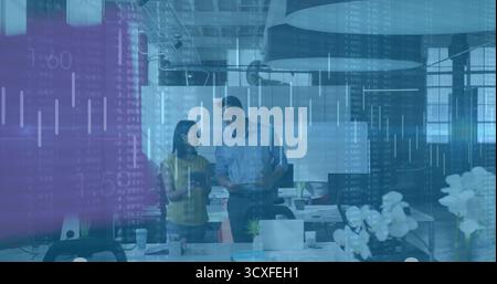 Two business professionals reviewing data overlay in open-plan workspace, with laptops Stock Photo