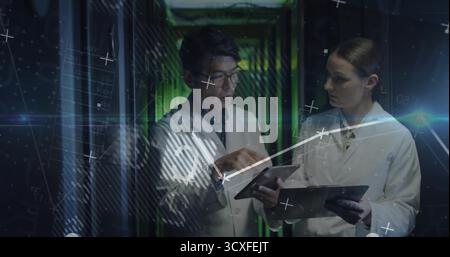 Monitoring IT engineers examining tablets and server racks in data center, with chart overlays Stock Photo