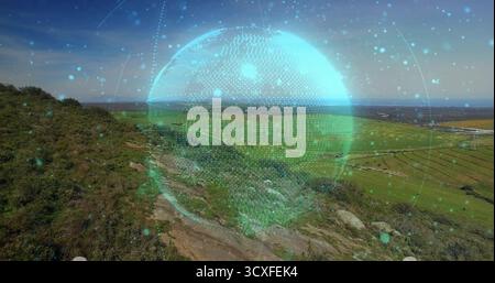 Displaying digital holographic globe floating above hillside, near rocky footpath toward farm plots Stock Photo