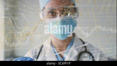 Female medical professional analyzing financial charts in corridor, wearing mask and stethoscope Stock Photo